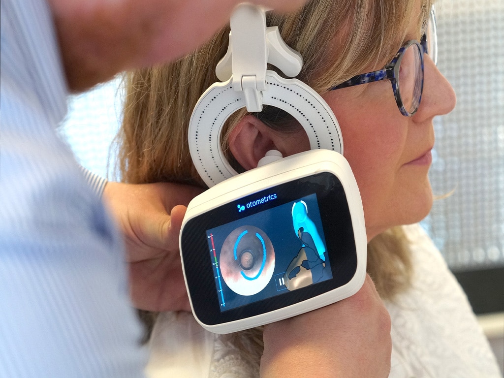 Ein Hörakustiker passt das Im-Ohr-Hörgerät einer Frau mithilfe eines Geräts an.